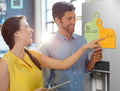 Man and woman looking at a refrigerator with a digital display, holding a colorful magnetic board.